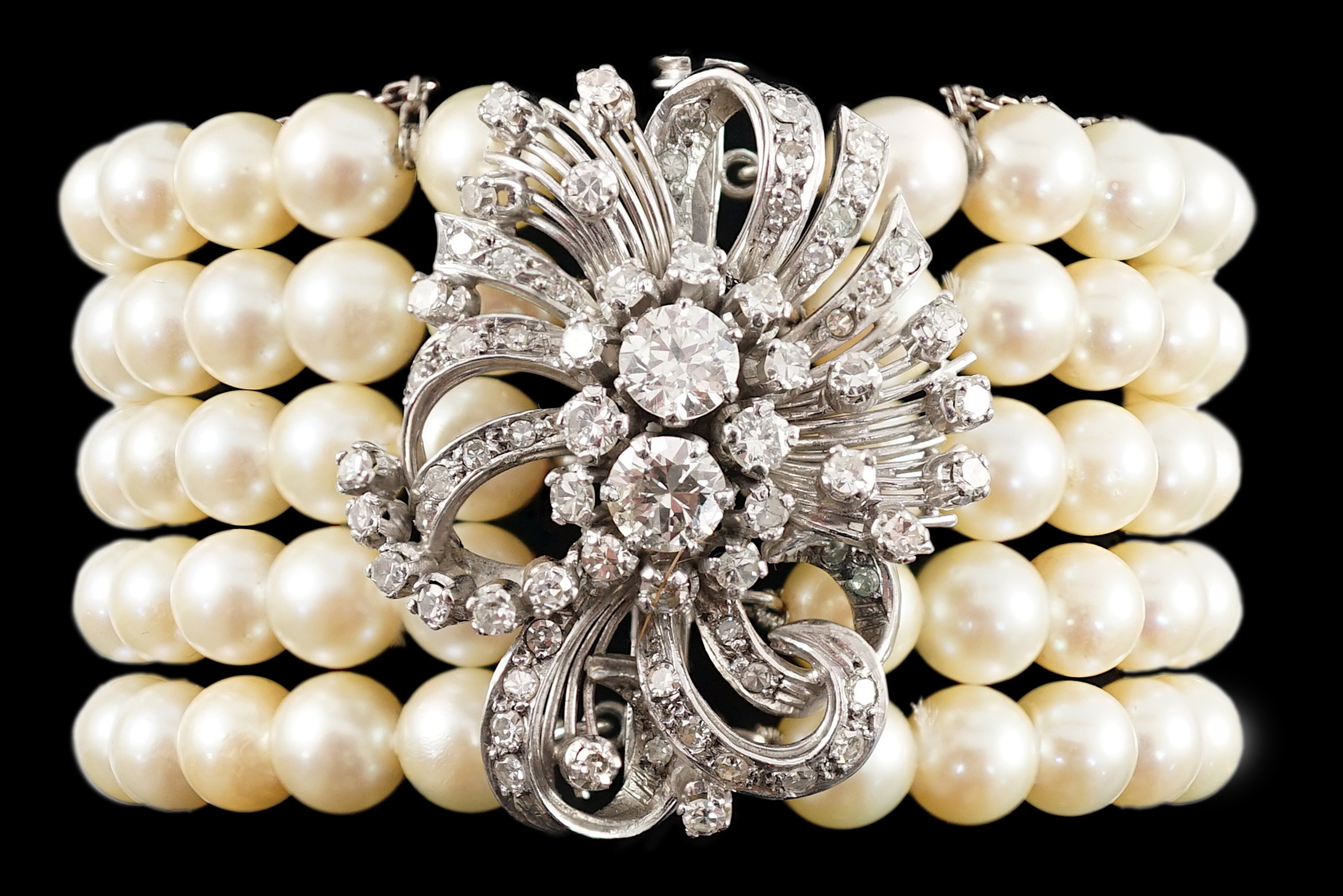 A mid to late 20th century continental quintuple strand cultured pearl bracelet, with white gold and diamond cluster set scroll clasp and diamond set line spacers